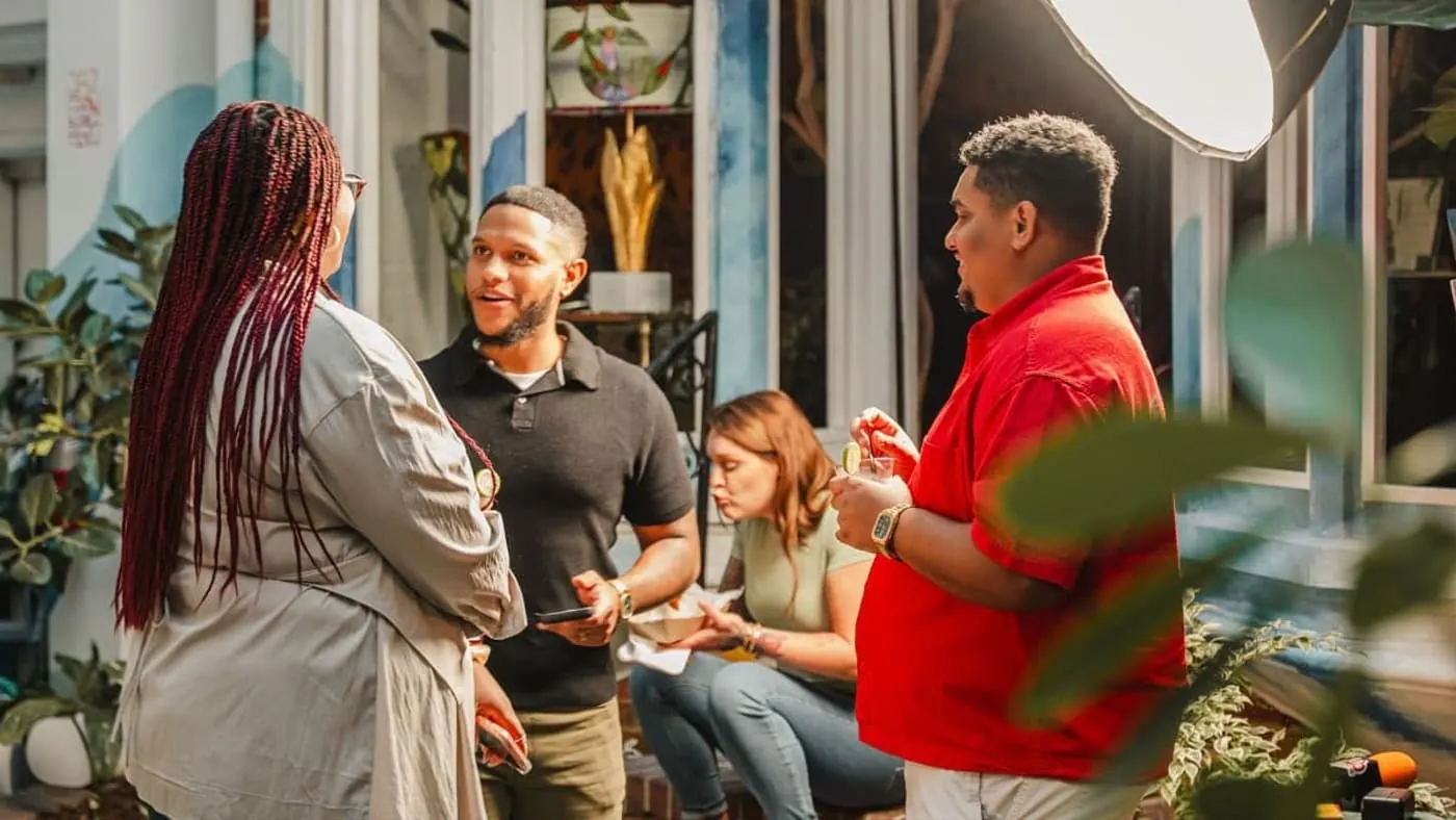 Four guests talking business in the courtyard at a Colado Latino Network gathering in Baltimore, drinks and plates in hand under the string lights at Stem and Vine