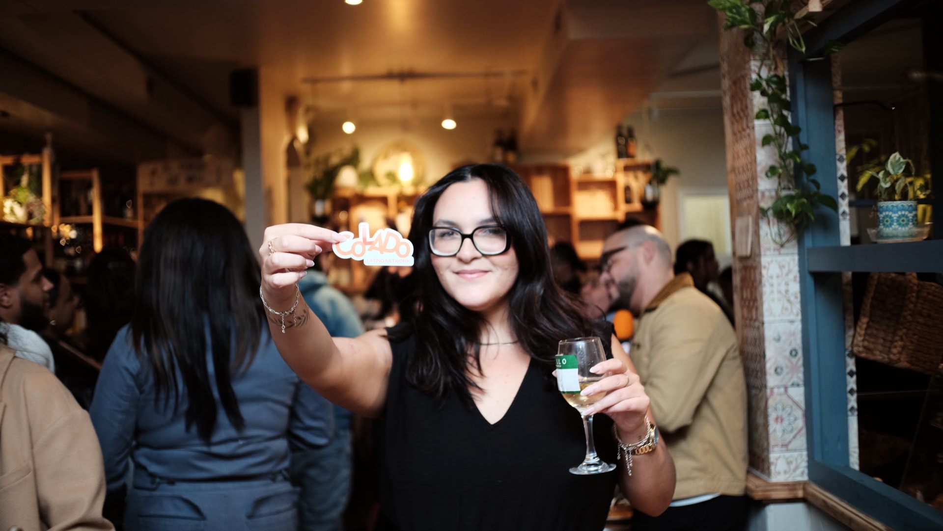 A guest at the first Colado Latino Network gathering holding a Colado sticker and a glass of wine inside Bodega and Vino, Baltimore