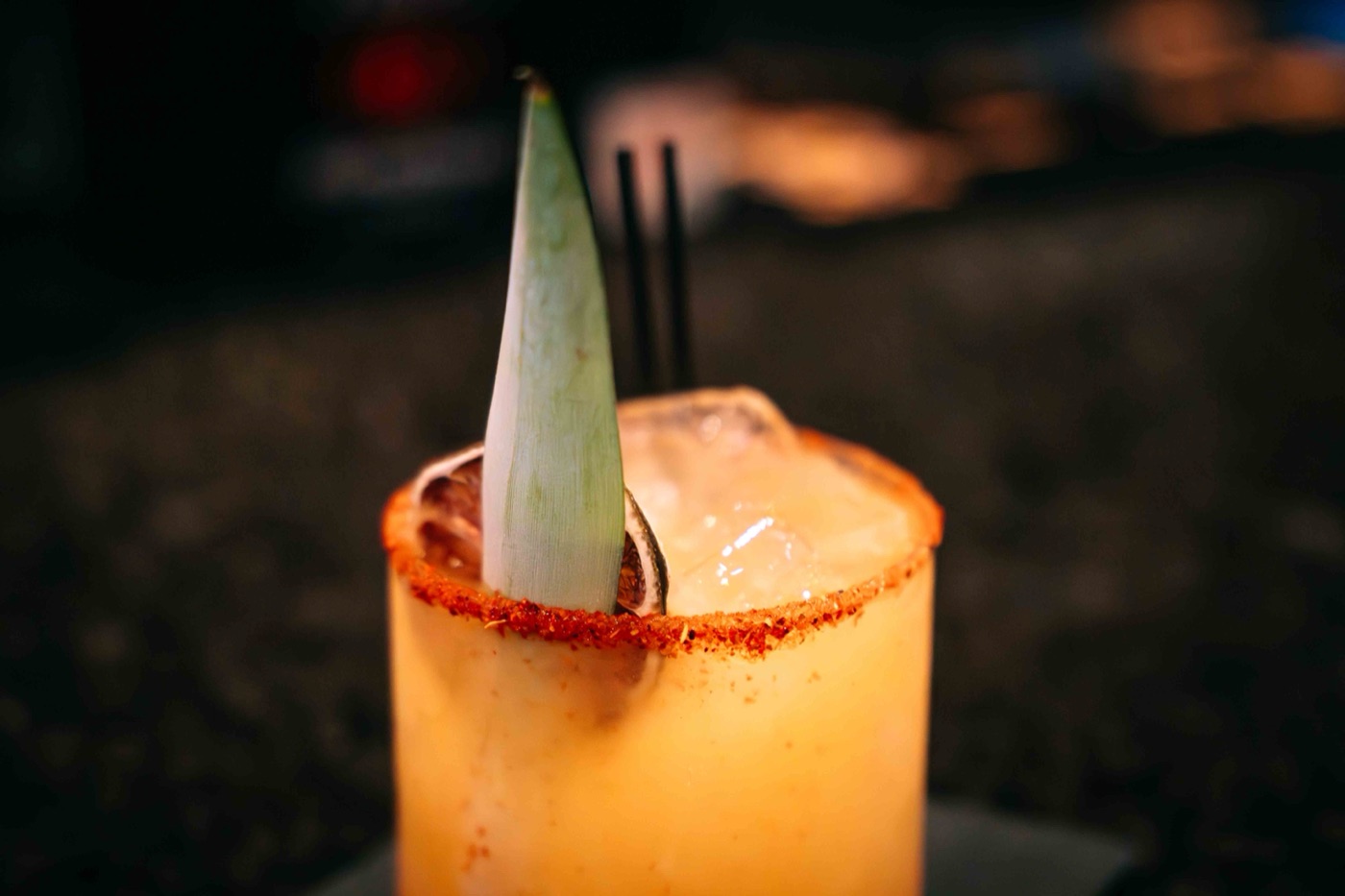 A close-up of The Empanada Lady's chili-rimmed signature cocktail with a pineapple leaf, served during the Colado Latino Network event in Baltimore