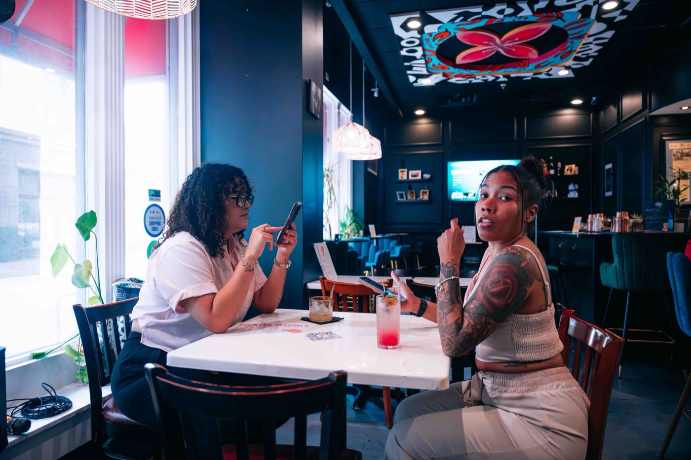 Two guests talking over cocktails at a table inside The Empanada Lady during the Colado Latino Network event in downtown Baltimore