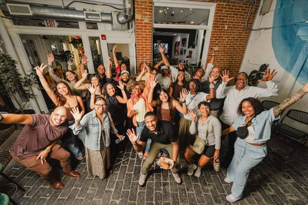 The full group at the Colado Latino Network event at Stem & Vine in downtown Baltimore, guests cheering with hands raised in the brick courtyard